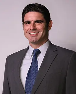 Man in suit smiling against plain background.